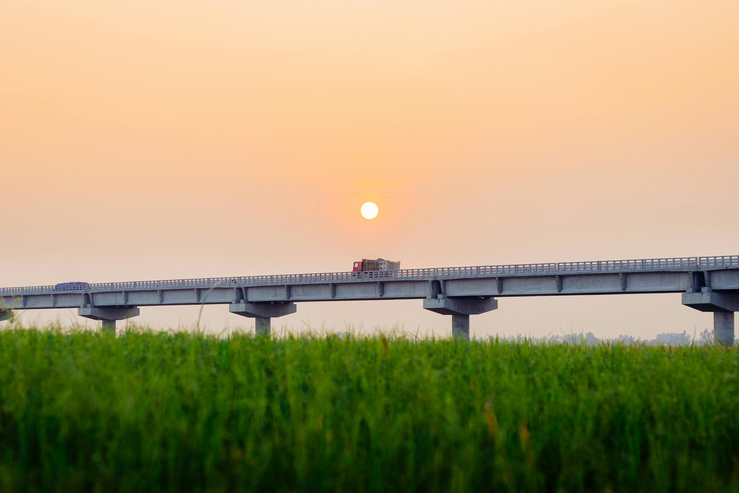 Tranquil sunrise over a scenic bridge with lush green fields in Chilmari, Bangladesh.